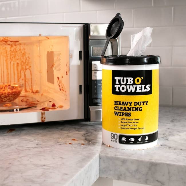The canister of wipes sitting next to a messy microwave