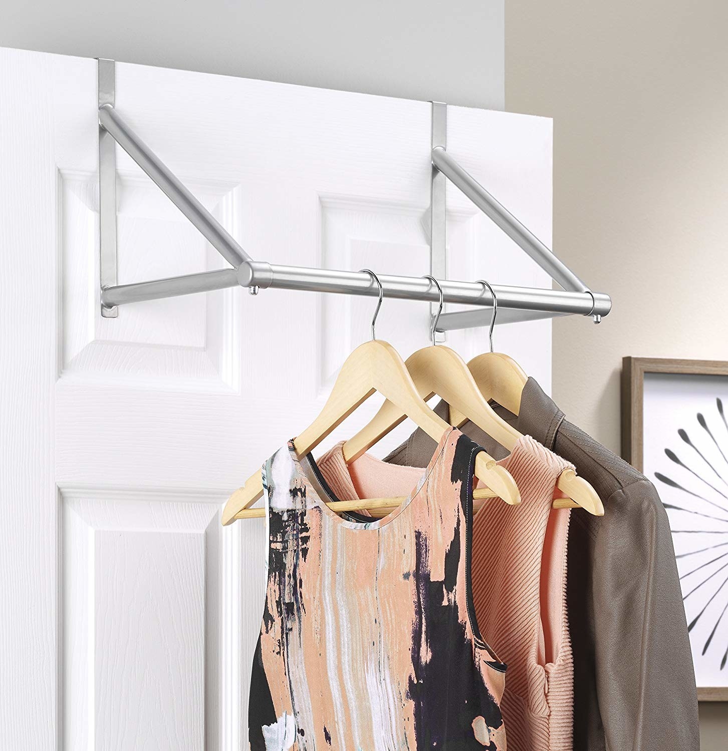 A metal clothing rod hanging from a door There are three hangers with two dresses and a jacket hanging from it