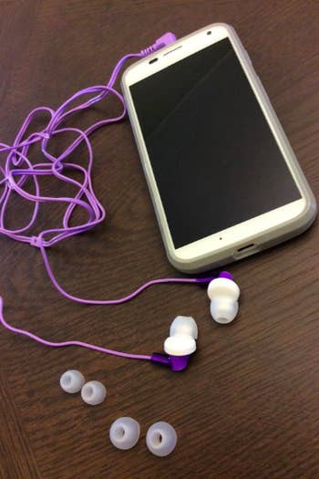 A reviewer's phone attached to the purple headphones, plus the extra, different-sized bud pads