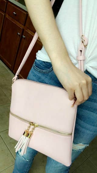 A reviewer carrying the bag in pale pink with a tassel zipper detail
