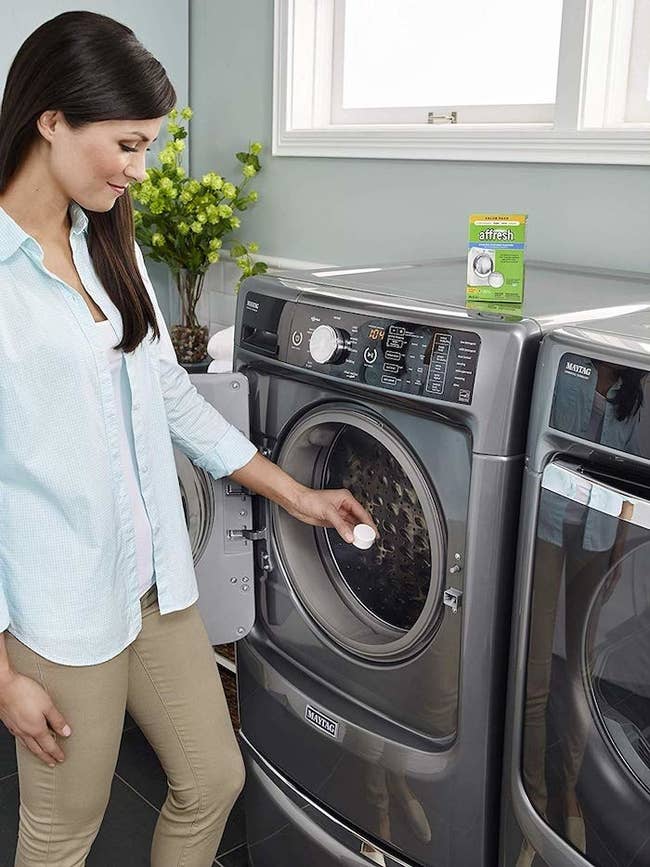 Product photo showing a model place Affresh washing machine tablets into their washing machine 