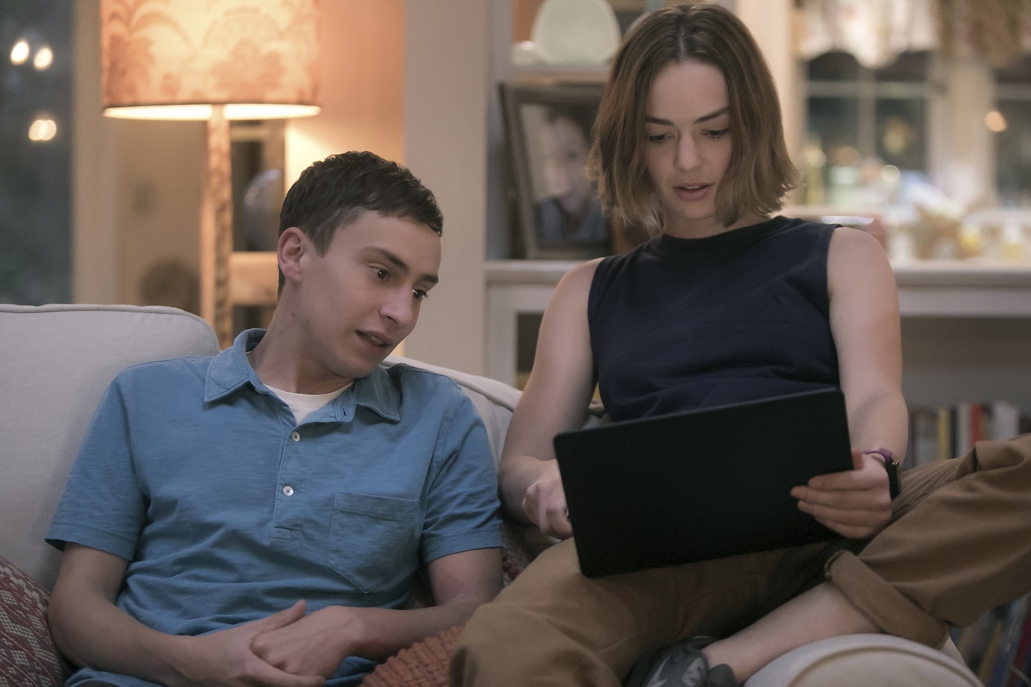 two of the characters looking at a tablet while sitting on the couch