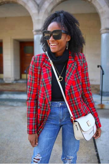 A reviewer wearing the red and green plaid blazer open with a turtleneck and ripped jeans