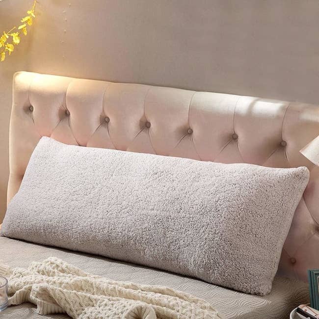Rectangular body pillow with a fuzzy cover in beige on a bed. 