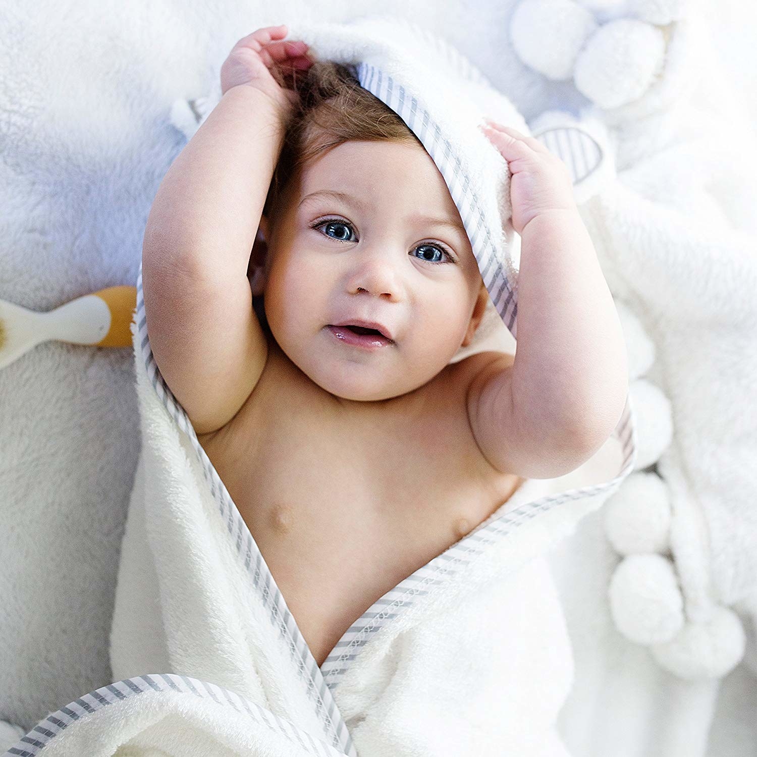 A baby lying down with a soft cotton towel around them The towel has a hood with ears 