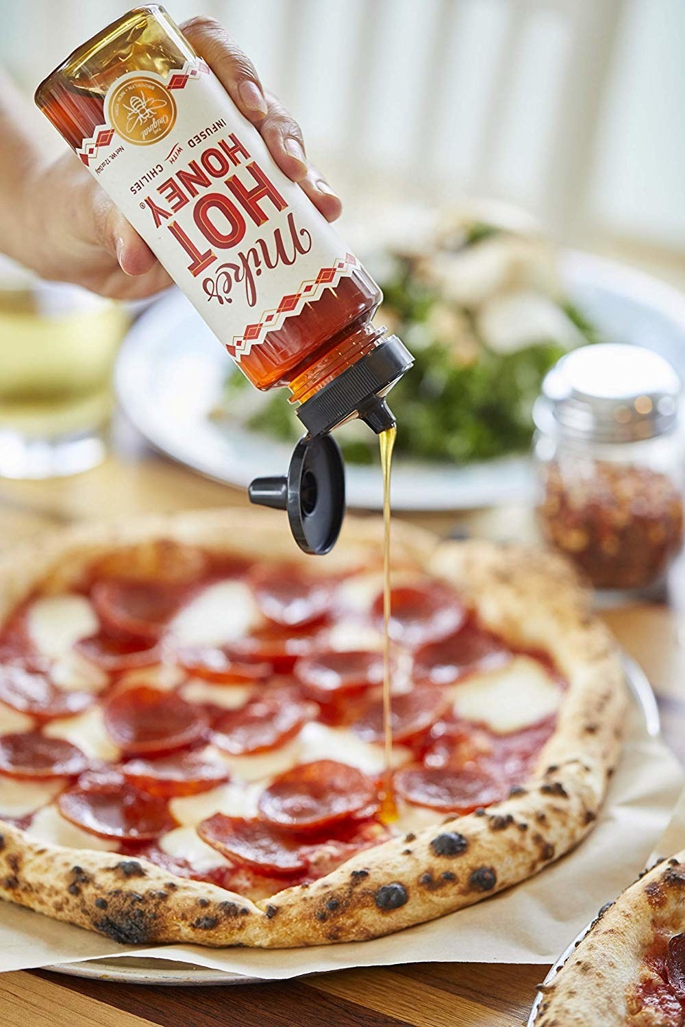 model pouring Mike&#x27;s Hot Honey on a pepperoni pizza