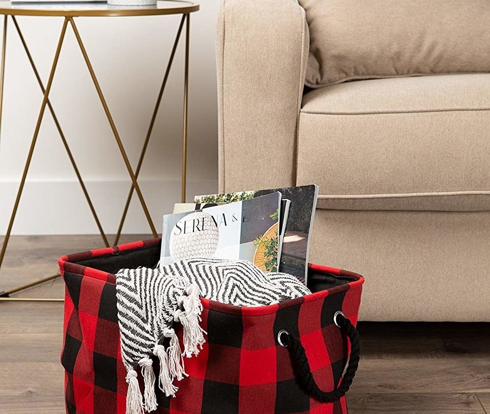 The black and red plaid storage bin filled with a blanket and magazines 