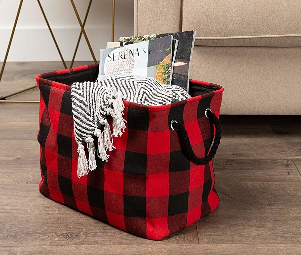 The black and red plaid storage bin filled with a blanket and magazines 