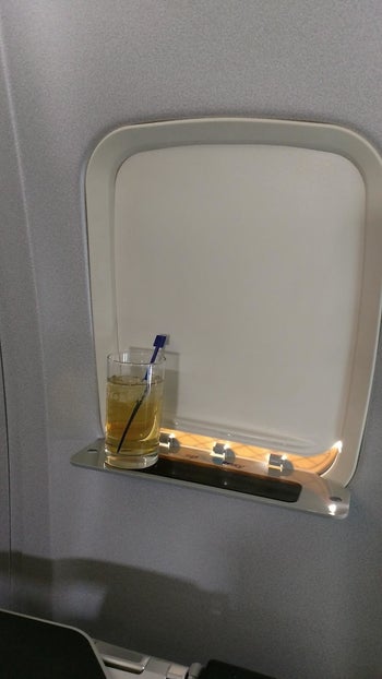 A reviewer's drink on the tray that is coming out of the plane's closed window