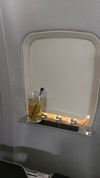A reviewer's drink on the tray that is coming out of the plane's closed window