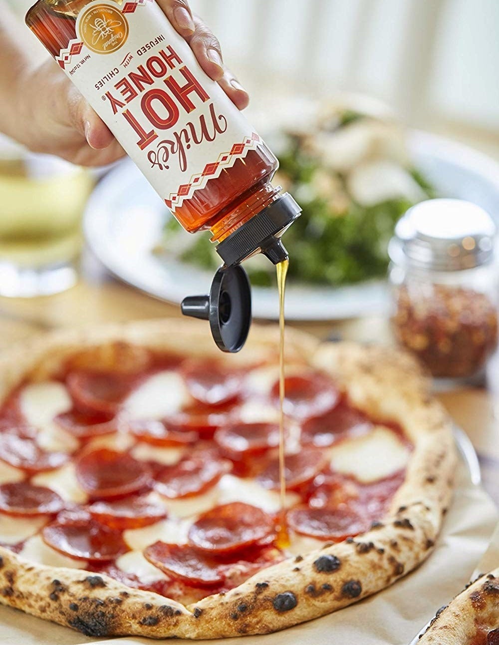 A bottle of Mike&#x27;s Hot Honey being poured onto a pizza. 
