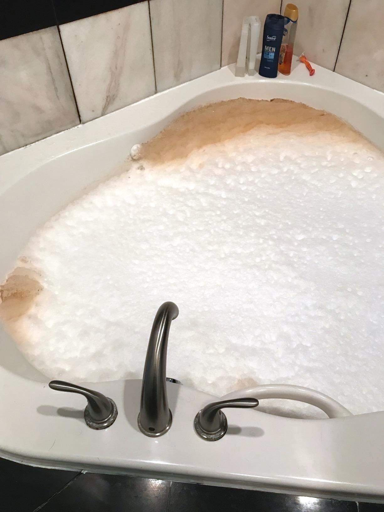 A reviewer&#x27;s tub filled with foam that&#x27;s mostly white but there&#x27;s big chunks of brown by the jets