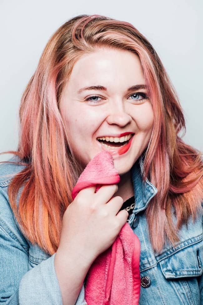 buzzfeed writer with half a face of makeup holding the pink makeup remover cloth