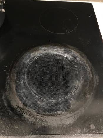 Before: reviewer's black glass cooktop with layers of brown and white cooked-on residue on the burners