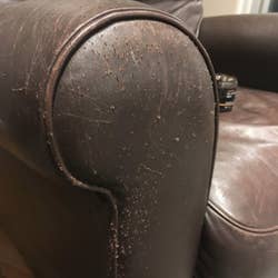 A reviewer's before: leather arm on a chair with lots of scratch marks on it