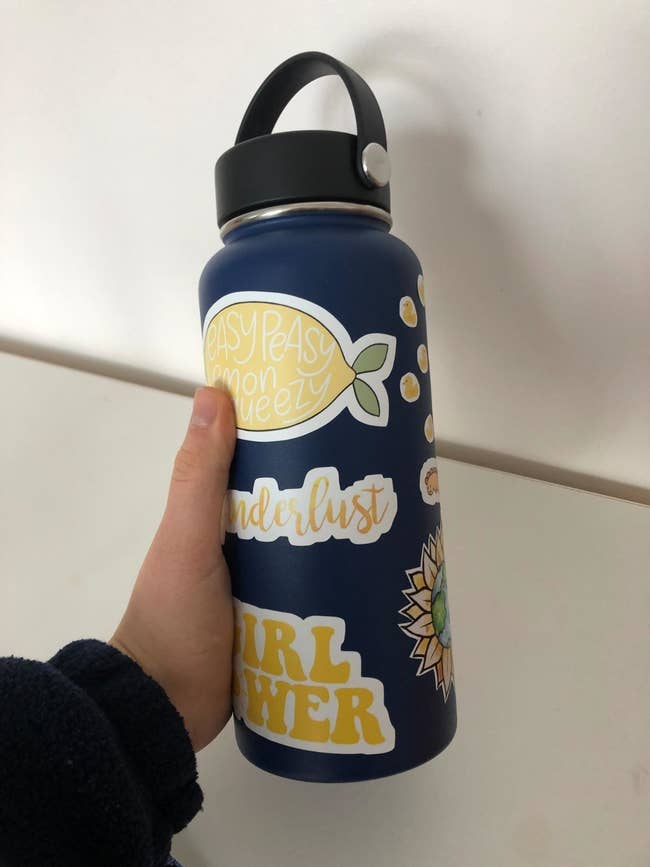 reviewer holding a navy hydro flask with stickers on it