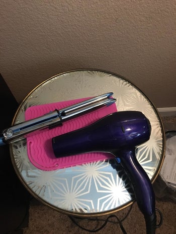 reviewer image of the pink silicone mat with a straightener and hair dryer sitting on it