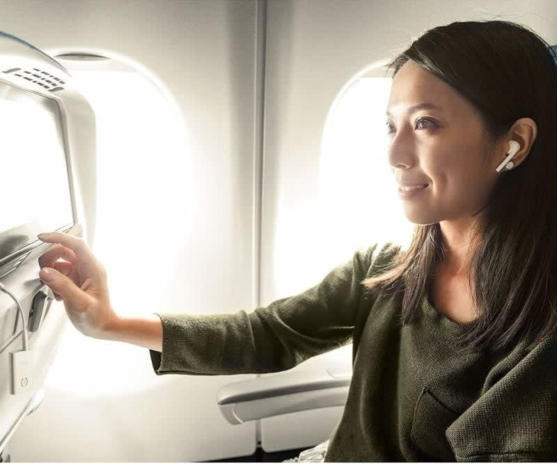 model with the small white box plugged into the screen on the seat back on a plane with wireless headphones in