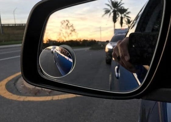 The blind spot mirror attached to a rearview mirror showing more closely, how much room is next to the car door