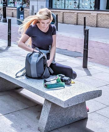Reviewer sitting on a bench with the gray backpack with a lighter gray stripe down the middle