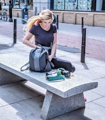 Reviewer sitting on a bench with the gray backpack with a lighter gray stripe down the middle