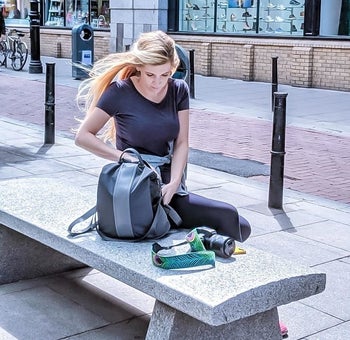 a reviewer sitting on a bench with the gray backpack with a lighter gray stripe down the middle