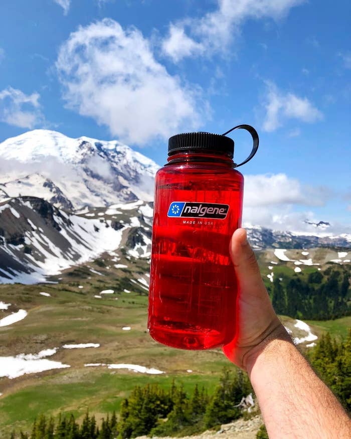 person holding red nalgene with mountain in the background