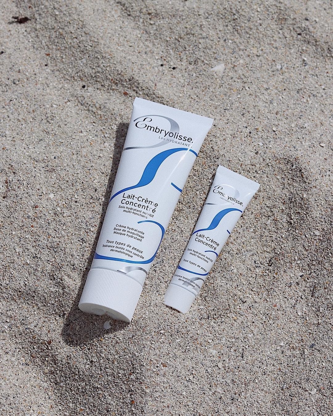 two tubes of the moisturizer on sand