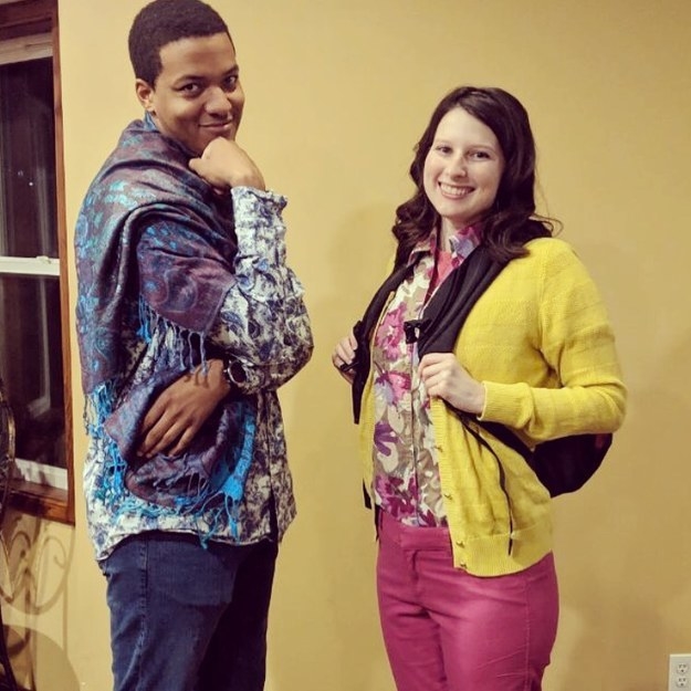 A man wearing a printed shirt and scarf draped around him. A woman is next to him with brightly printed clothes and a backpack. 