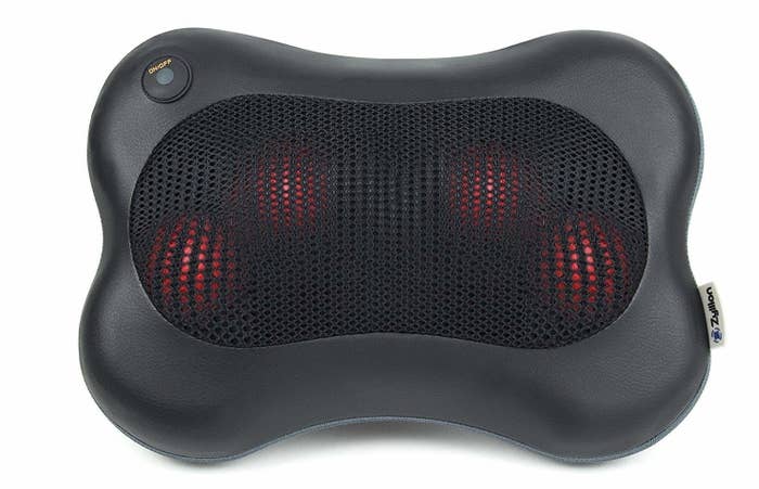 The massager, which is almost shaped like a squashed dog bone, with four rounded corners; it has four red balls protruding from under mesh in the center, and a power button