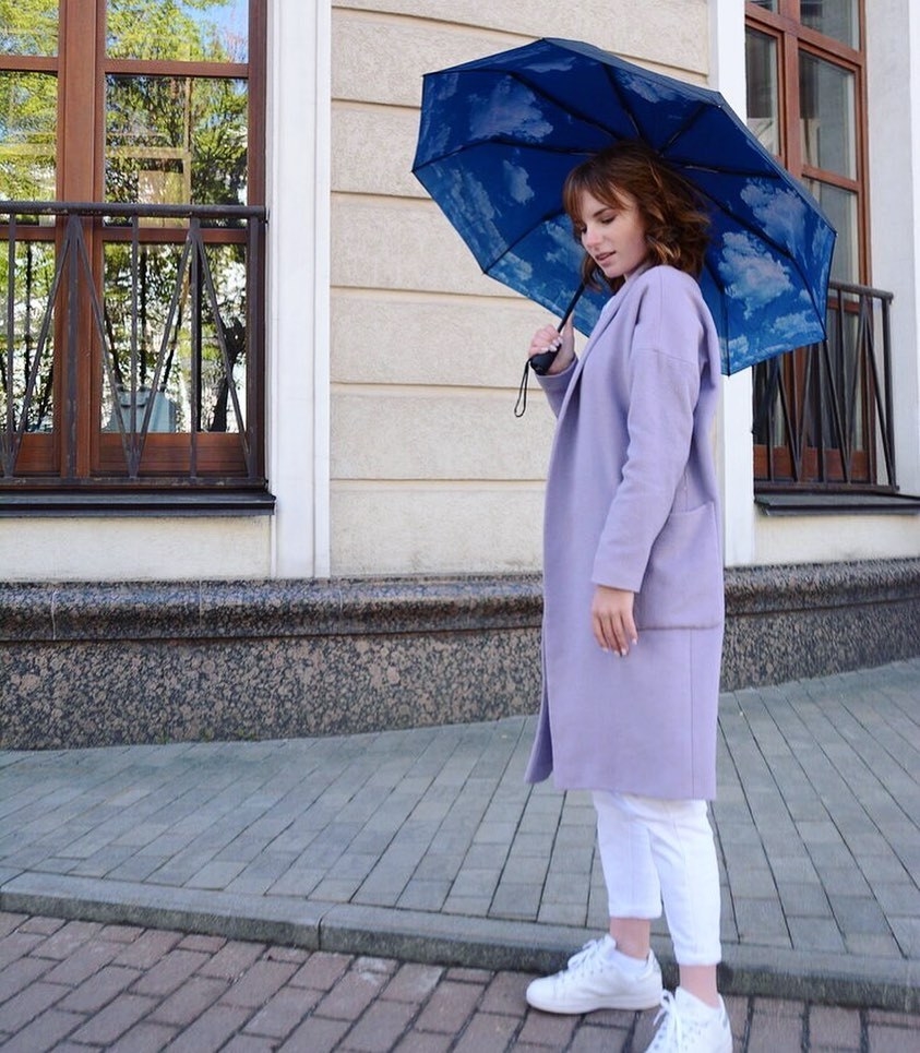 A photo of a model using the umbrella in blue with a cloud design on the inside of the umbrella