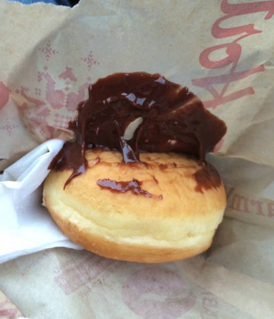 A donut with chocolate spread on top, partially wrapped in paper