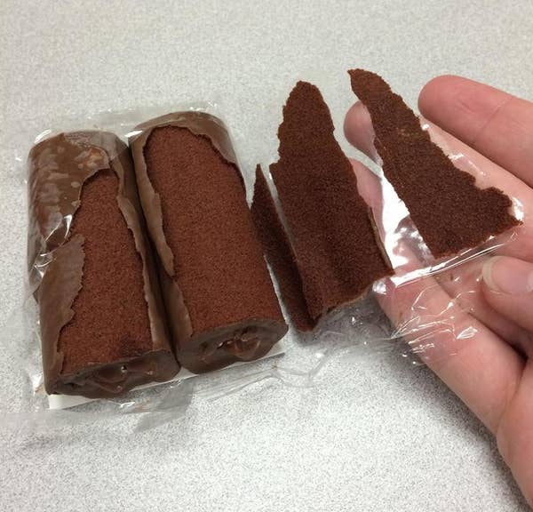 Two half-eaten chocolate cake rolls with the outer chocolate layer peeling off, held in a hand