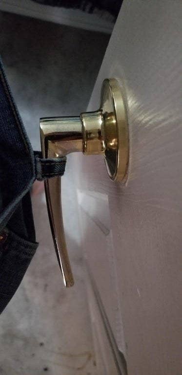 A brass door handle secures the corner of a pair of jeans caught between the latch and the wall