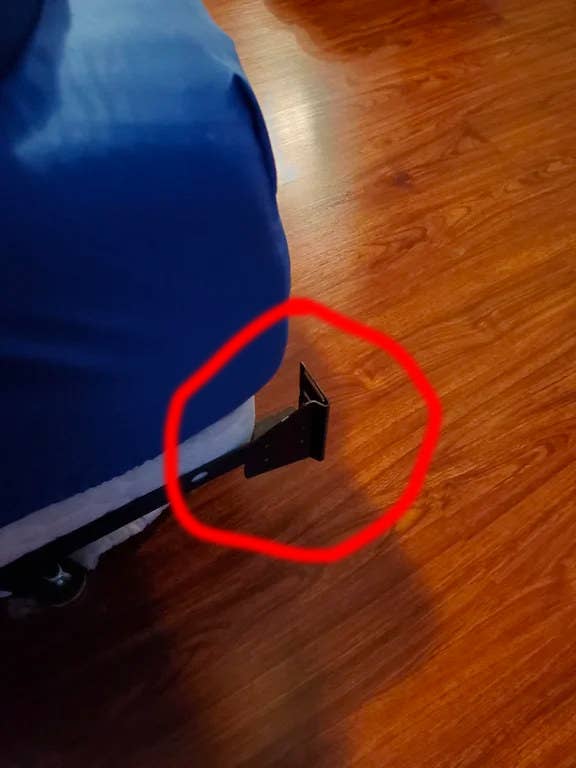 Bedframe leg protruding from the side of a bed on a wooden floor, encircled in red