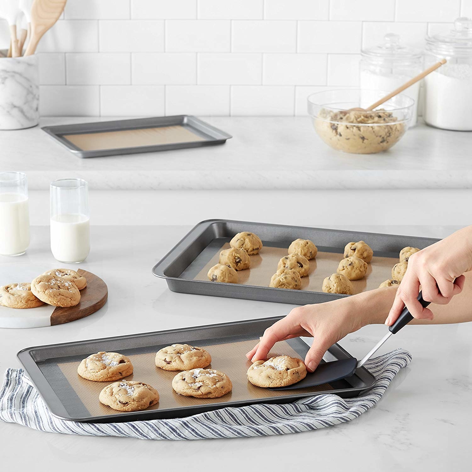 A person picking up a cookie from a baking tray with a kitchen spatula The baking tray is line with a silicone mat