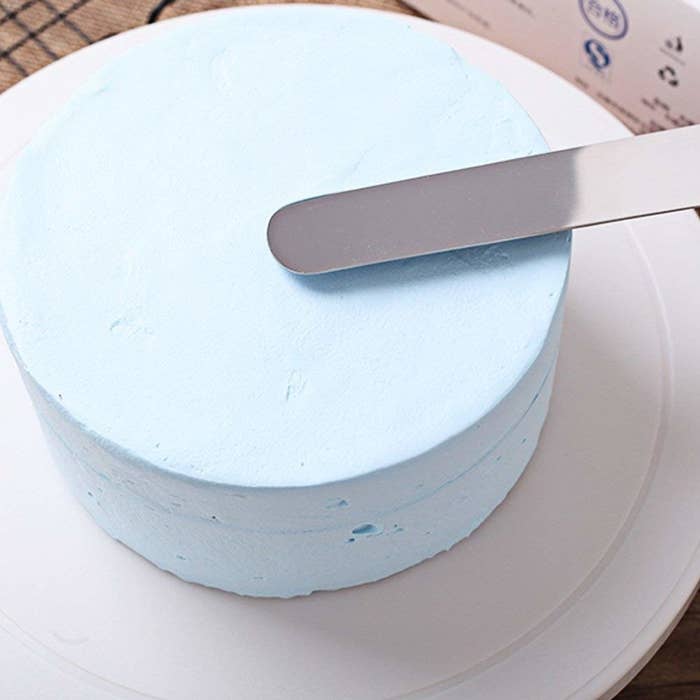 A person icing a cake with a metal spatula