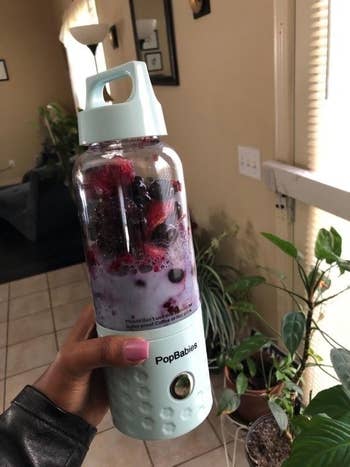 A reviewer holds their personal blender which is full of berries