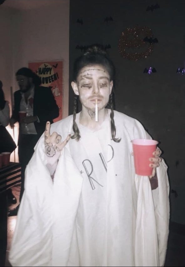 A person in a white sheet titled &quot;RIP&quot; with Post Malone&#x27;s face and hand tattoos