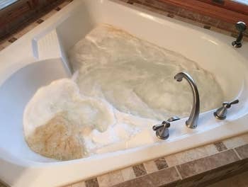 reviewer's bath tub with the soapy cleaner in it and dirty bubbles where the jets are 