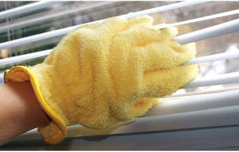 Person wearing glove and cleaning blinds between their fingers 