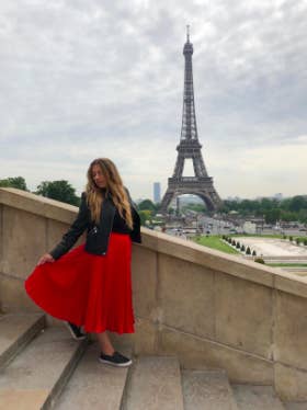 another reviewer wearing the red skirt with black sneakers and a black moto jacket with a view of the Eiffel Tower in the background