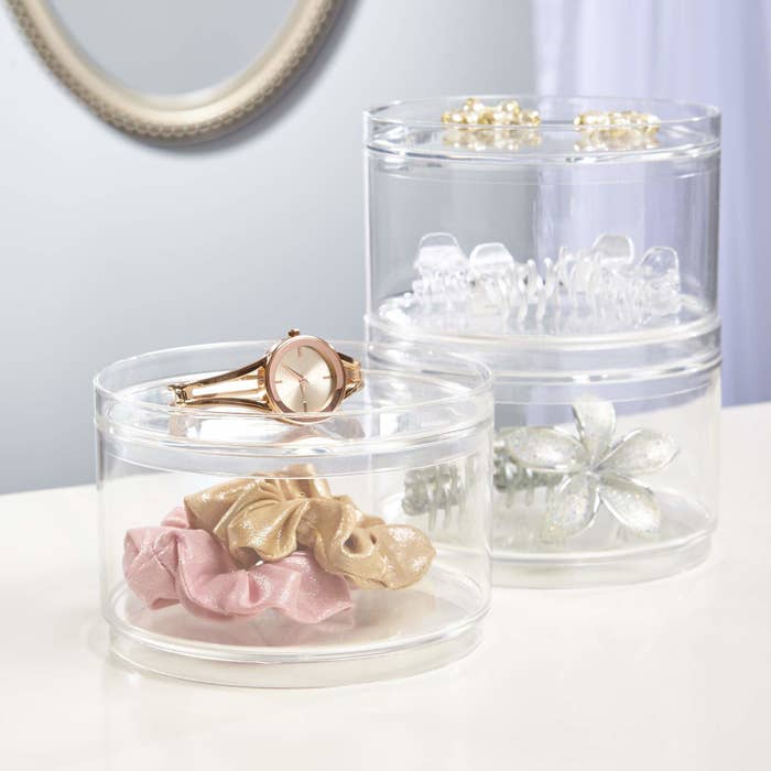 Circular see-through containers holding hair accessories. The containers can stack on top of each other