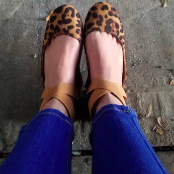 A reviewer wearing the flats with criss-cross ankle straps in leopard
