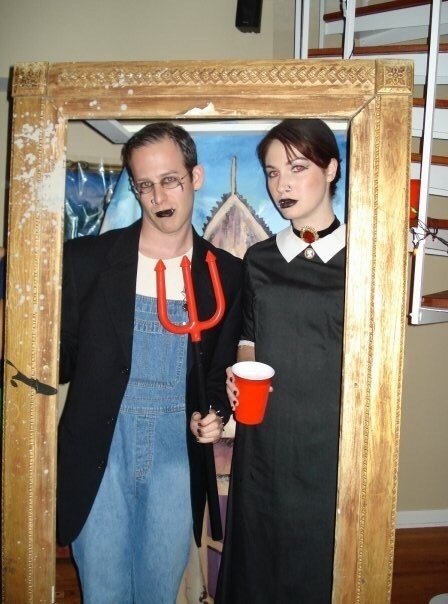 Two people inside a large frame recreating the &quot;American Gothic&quot; painting with goth clothes and makeup