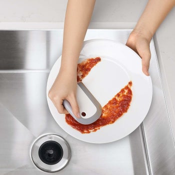 A hand using the tool to scrape sauce off a plate