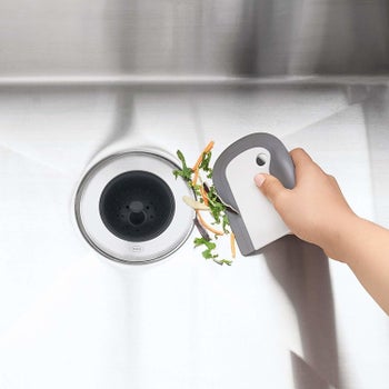 A hand using it to push scraps down a garbage disposal