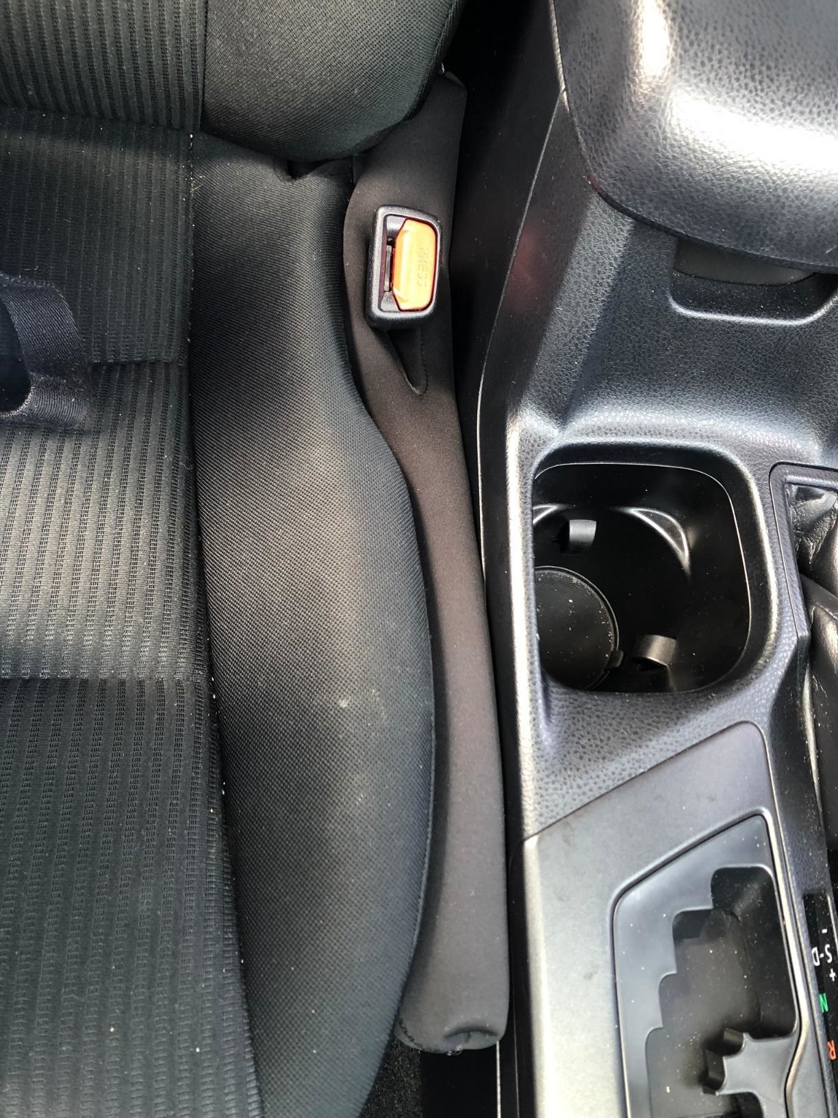 reviewer&#x27;s drop stop squished between their passenger seat and cup holder