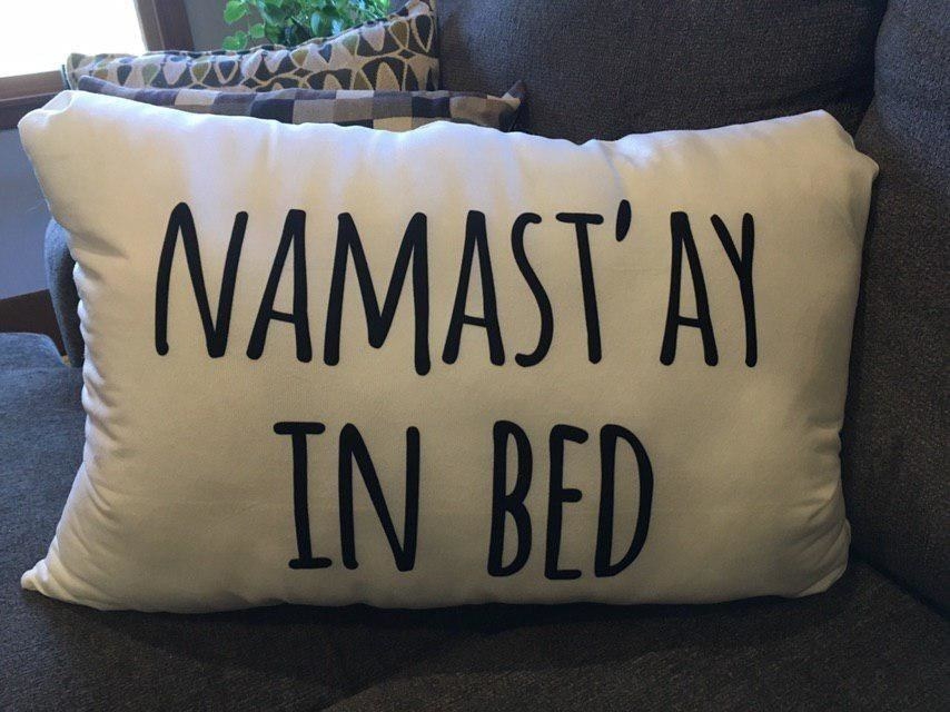 Reviewer pic of the small rectangle white throw pillow with the words &quot;Namast&#x27;ay in bed&quot; written in black