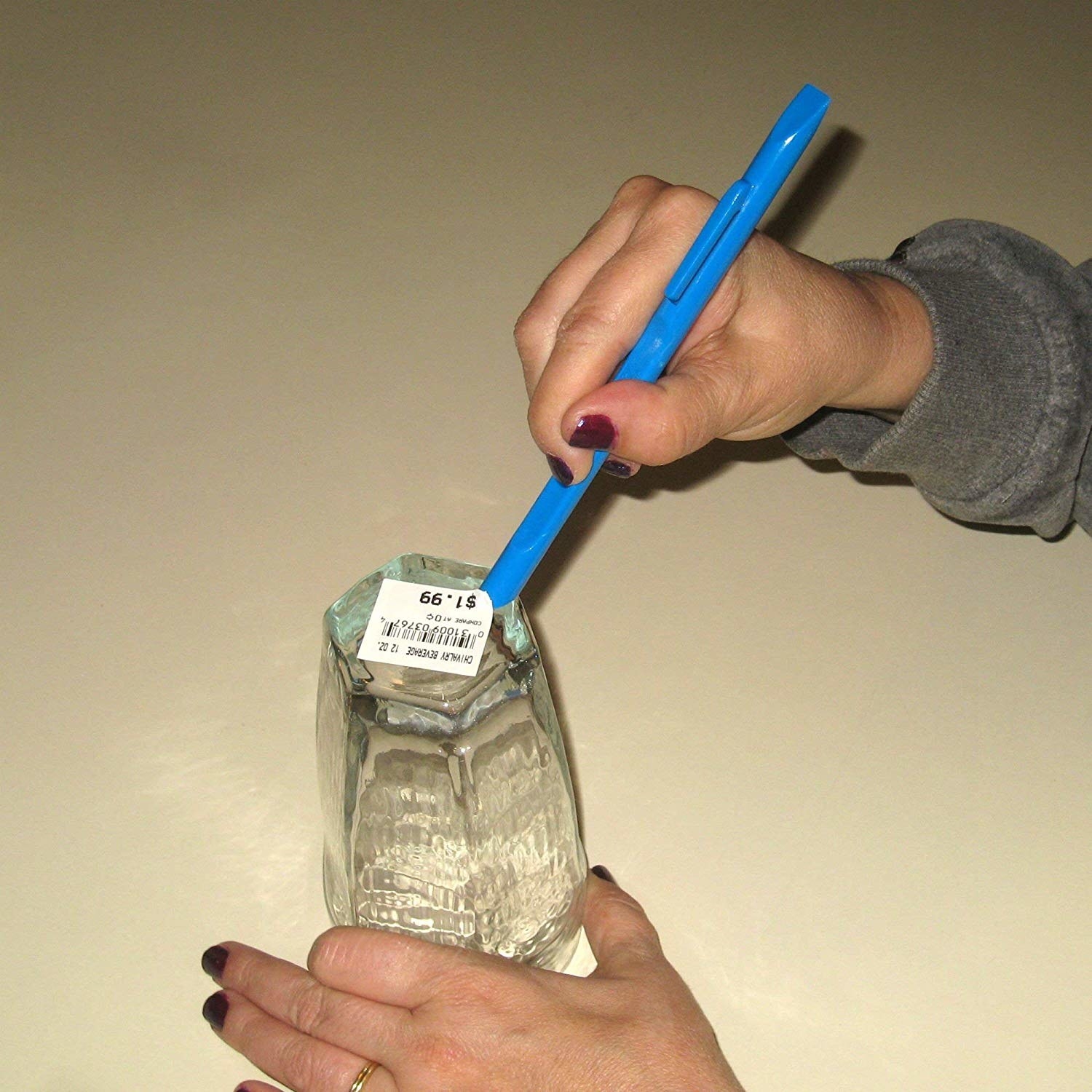 A hand using the scraper to remove a sticker from a glass